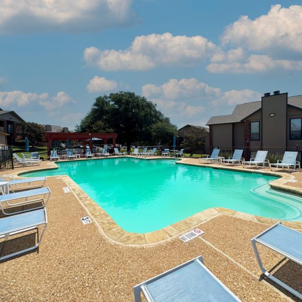 Valley Creek Outdoor swimming pool with clear blue water, surrounded by a concrete deck, lounge chairs, and red brick buildings.
