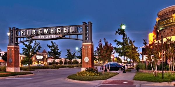Valley Creek Firewheel Town Center entrance with lit signs and trees at dusk.
