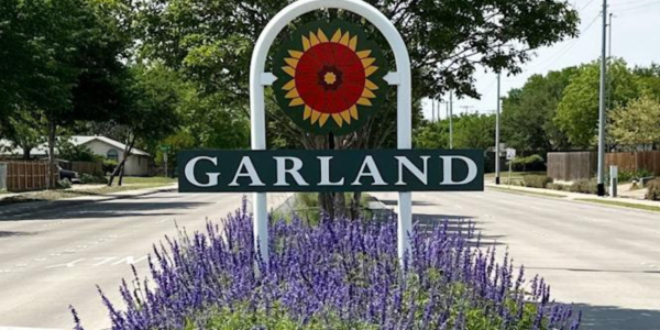 Valley Creek Welcome sign for Garland with a sunflower design and purple flowers in the foreground.