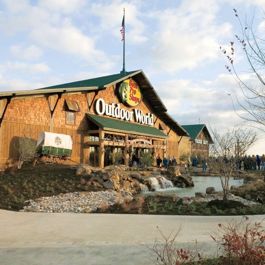 Valley Creek Bass Pro Shops Outdoor World store with a landscaped entrance and trees under a partly cloudy sky.