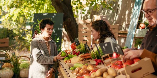 Valle Creek Two women and a man at an outdoor market stand with fresh vegetables and fruits.
