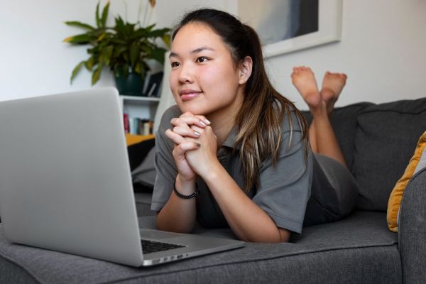 Valley Creek Person lying on a couch, looking at a laptop screen, with hands clasped under chin. A plant is in the background.